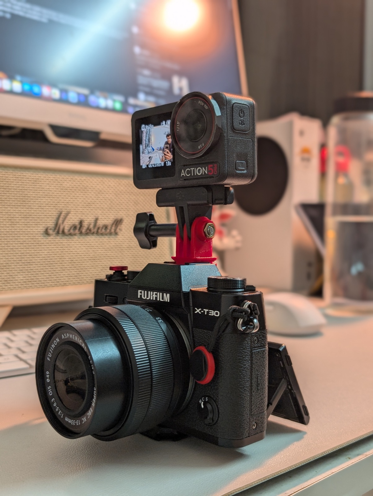 Close-up of the rig on the desk: Fujifilm X-T30 III with the DJI Action 5 Pro riding on its hotshoe via the red printed adapter